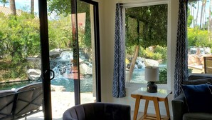 Une pièce dotée d’une grande fenêtre donnant sur une cascade et une végétation luxuriante. On y trouve une petite table avec une lampe, ainsi qu’un canapé agrémenté de coussins.