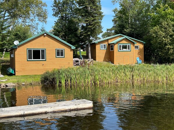 Two wooden cabins by a calm lake with a dock, surrounded by tall trees and reeds. - Cozy All Season House on Rangeley Lake (Rangeley)