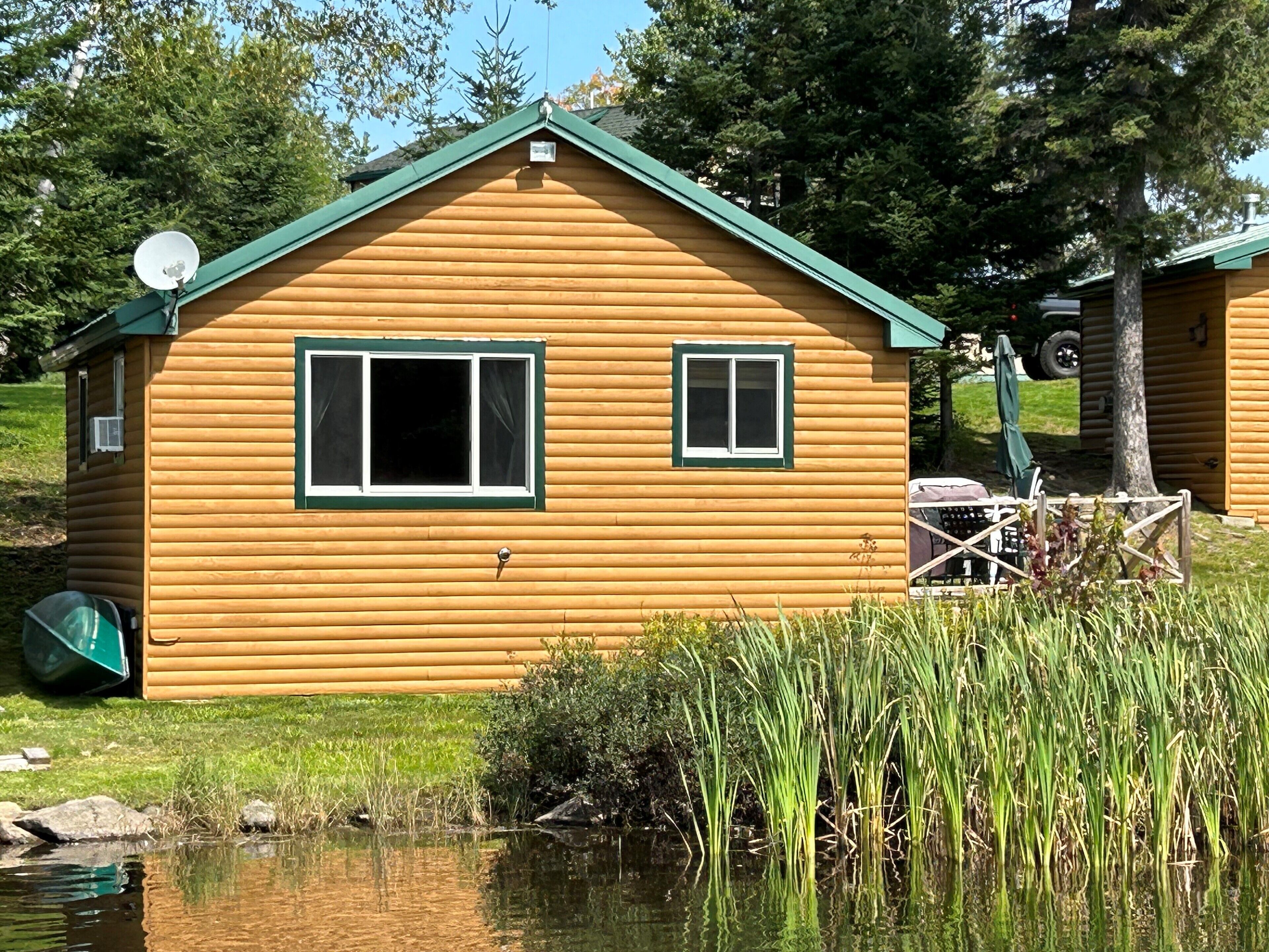 A wooden cabin with a green roof, two windows, and a satellite dish.