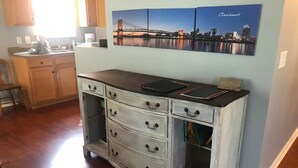 Een keuken met een witte kast, een zwart aanrechtblad en een stadslandschap schilderij aan de muur.
