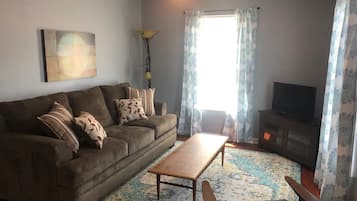 A living room with a sofa, a coffee table, a TV, and a patterned rug.