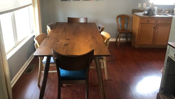 Een eetgedeelte met een houten tafel en stoelen, een stadsgezichtschilderij erboven en een keuken met houten kastjes en een spoelbak.