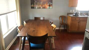 A dining area with a wooden table and chairs, a cityscape painting above the table, and a kitchen area with wooden cabinets and a sink.