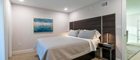 A bedroom with a bed, a nightstand, a painting, and a door leading to another room.