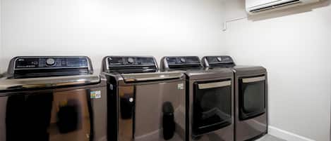 A laundry room with four stainless steel appliances, a white wall, and an air conditioning unit.