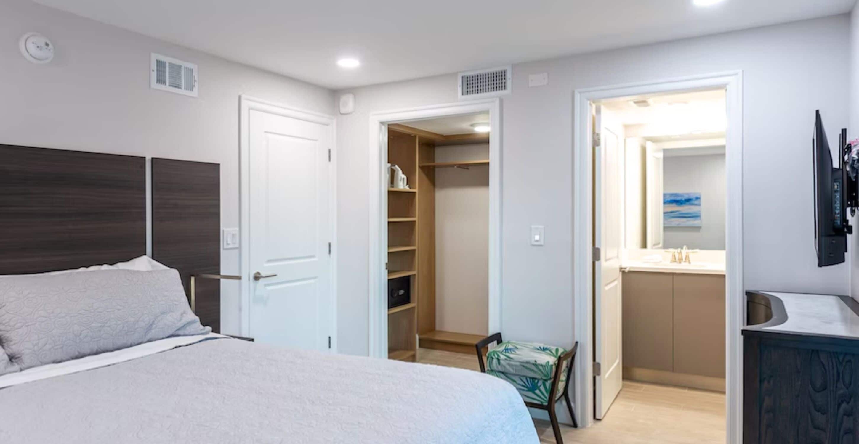 A bedroom with a bed, a closet, a bathroom, and a small seating area.