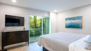 A bedroom with a bed, a TV mounted on the wall, a painting, and a balcony with a view of greenery. - Wiggins Pass Chalet (Naples)