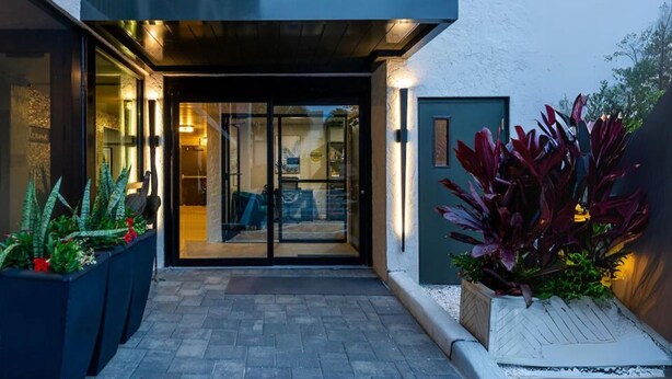 A modern building entrance with glass doors, a dark exterior, and potted plants on the sides. - Wiggins Pass Chalet (Naples)