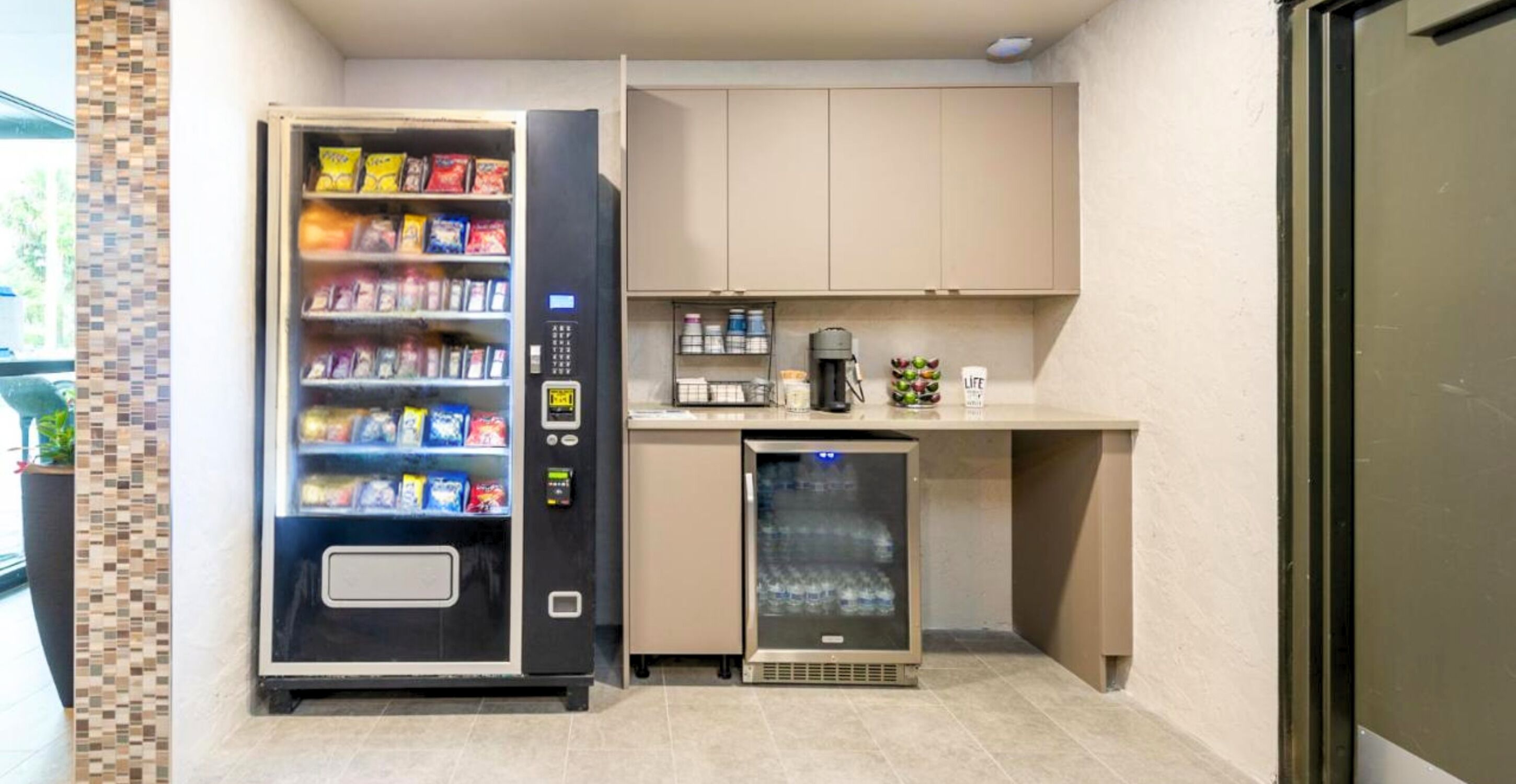 Eine kleine Küchenzeile mit einer Getränkeautomaten, einer Kaffeemaschine und einem kleinen Kühlschrank.