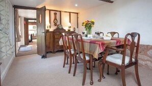 Un coin repas avec une table dressée pour quatre personnes, des chaises en bois, une horloge et un vase de fleurs.