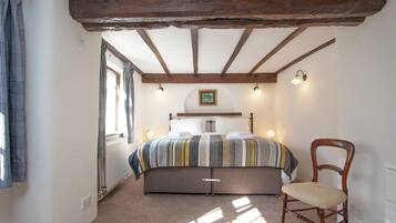 A bedroom with a bed, a chair, a window, and a ceiling with exposed beams.