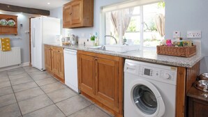 Une cuisine avec des meubles de rangement en bois, un lave-linge encastré, un plan de travail avec un évier et une fenêtre avec des rideaux.