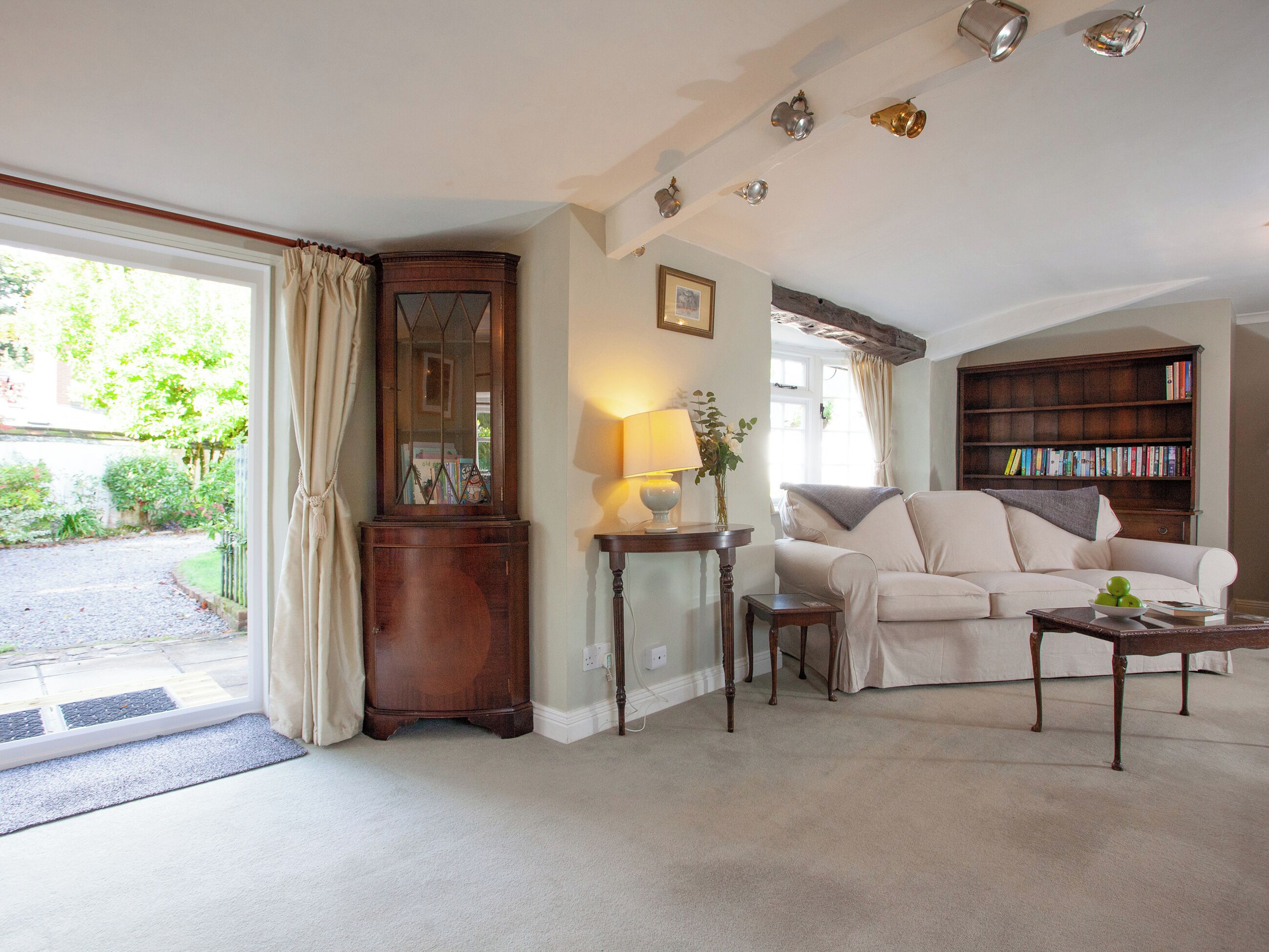 A living room with a sofa, a wooden cabinet, a lamp, a bookshelf, and a window with curtains.
