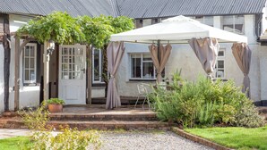 Un bâtiment doté d’un patio couvert, d’une porte et d’un petit jardin avec des plantes.