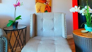A room with a tufted armchair, a surfboard with an octopus design, and two potted orchids. - NEW! Modern 2bd/2ba Beach Retreat in Sunny South Kihei (Kihei)