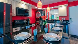 A modern kitchen with stainless steel appliances, a central island with dining setup, and red accent walls. - NEW! Modern 2bd/2ba Beach Retreat in Sunny South Kihei (Kihei)