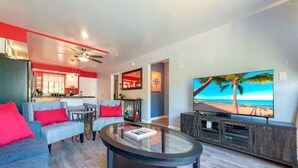 A modern living room with a glass coffee table, grey sofas with red cushions, a flat-screen TV, and a kitchen in the background. - NEW! Modern 2bd/2ba Beach Retreat in Sunny South Kihei (Kihei)
