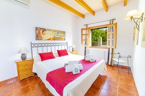 Une chambre spacieuse avec un grand lit, une tête de lit en bois, une fenêtre avec des volets ouverts, une table de chevet avec une lampe et un tableau accroché au mur.