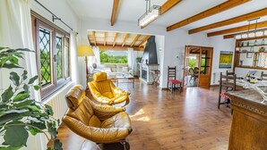 A spacious living area with wooden beams, a fireplace, and a view of greenery. - Villa Ca na Quarta (Alcúdia)