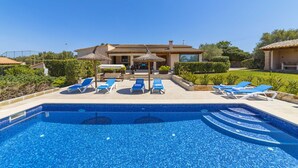 Una piscina con azulejos azules, rodeada de sillas de descanso y sombrillas.