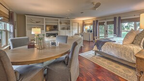 A spacious living room with a wooden dining table, comfortable seating, a large bed with a patterned bedspread, and a television on a built-in shelf.