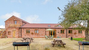 Een gebouw van baksteen met een rode dakbedekking, een houten trap en een terras met picknicktafels en een barbecue.