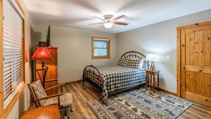 A bedroom with a bed, a ceiling fan, a window, a door, and a chair.