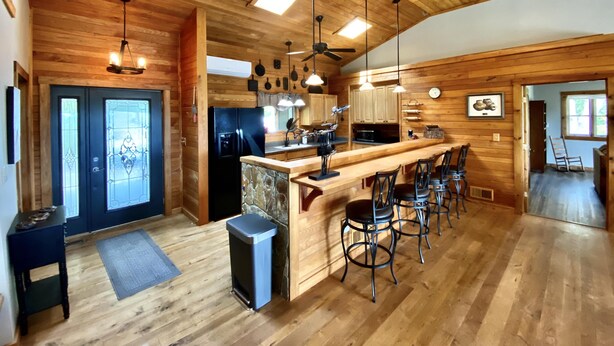 A spacious kitchen with wooden walls, a central island with bar stools, and a large refrigerator.