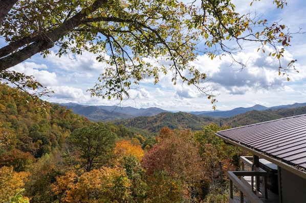 A view of a mountainous landscape with autumn foliage, a wooden deck, and a building with a metal roof. - Stunning Mtn Views/Private/Sparkling Hot Tub/WI-FI (Bryson City)
