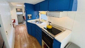 A compact kitchen with blue cabinets, a black stove, and a yellow kettle. - The Austin LoveStream! New Hot Tub, Full Bathroom, Deck & Grill! (Austin)
