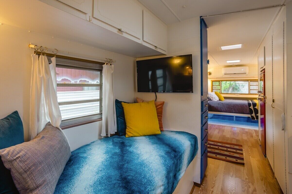 A compact living space with a bed, a sofa, a television, and a window with curtains.