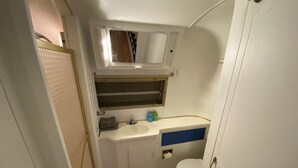 A compact bathroom with a white sink, a mirror above it, a toilet, and a small window. - The Austin LoveStream! New Hot Tub, Full Bathroom, Deck & Grill! (Austin)