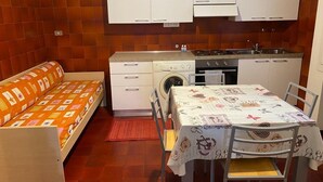A compact kitchen with white cabinets, a washing machine, and a dining table with a floral tablecloth. - RES Falena apartment within walking distance of the hospital and the city center (Padova)