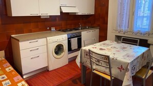 A compact kitchen with white cabinets, a washing machine, a stove, and a dining table with a floral tablecloth. - RES Falena apartment within walking distance of the hospital and the city center (Padova)