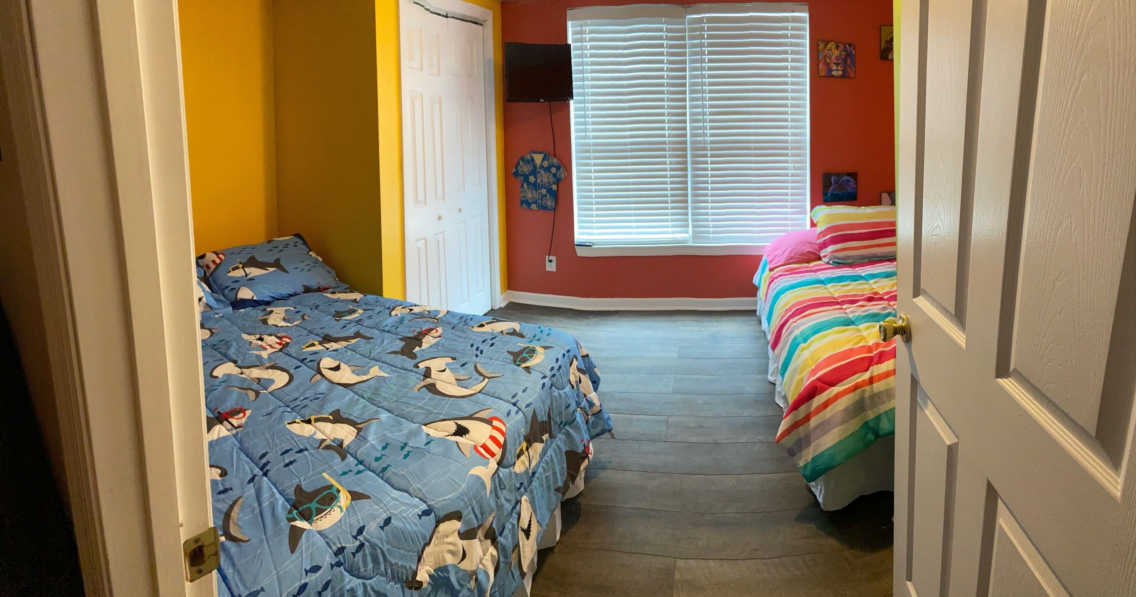 A narrow hallway with two beds, one with a blue shark-themed bedspread and the other with a rainbow-striped bedspread.