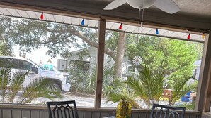 A covered patio with a table and chairs, a ceiling fan, and a view of the street and greenery outside. - Lower Level, Apartment Style Beach House! (Surfside Beach)