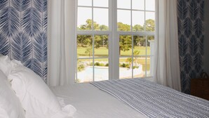 A bedroom with a large window, a bed with white bedding, and patterned curtains. - Luxury villa in beautiful Brunswick Plantation. Sunset Beach/Ocean Isle/Calabash (Calabash)