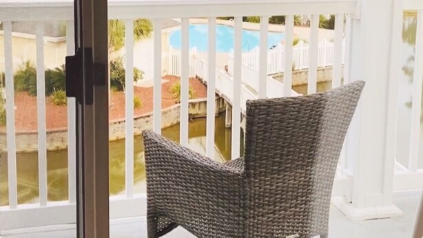 A wicker chair on a balcony with a view of a swimming pool and a grassy area. - Luxury villa in beautiful Brunswick Plantation. Sunset Beach/Ocean Isle/Calabash (Calabash)