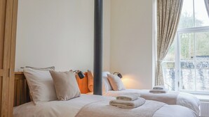 Habitación de hotel con dos camas, un ventanal grande con cortinas y una puerta de madera.
