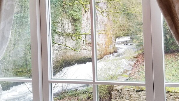 Una ventana con vista a un arroyo rocoso y árboles.
