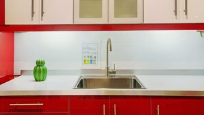 Una cocina con gabinetes blancos, un lavamanos de acero inoxidable y un jarrón decorativo verde.