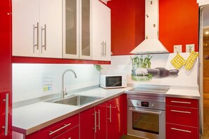 A modern kitchen with red cabinets, a stainless steel sink, a microwave, and an oven.