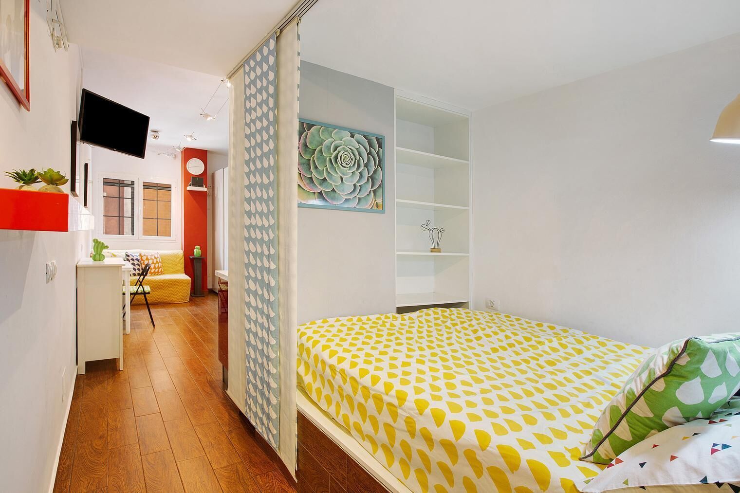 Quarto compacto com cama, escrivaninha, cadeira e televisão.