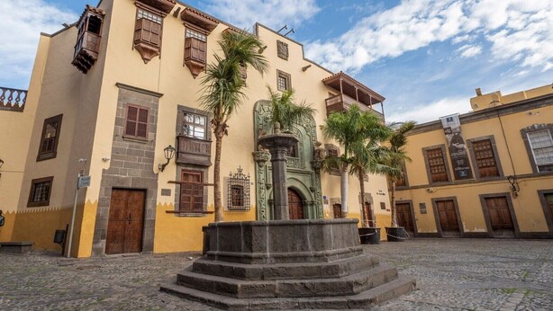 Un patio con una fuente central, suelo de adoquines y edificios de arquitectura tradicional.