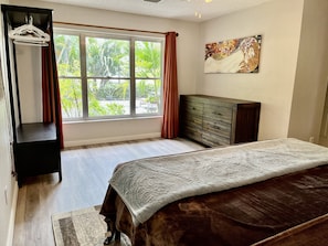 Un dormitorio con cama, cómoda, armario y ventana con cortinas.