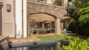 A pool with a stone archway, a dining area with outdoor furniture, and lush greenery.
