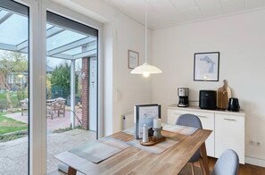 A dining area with a table, chairs, a coffee machine, and a view through a glass door to an outdoor patio.