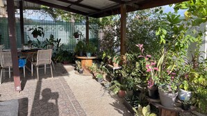 Ein überdachter Patio-Bereich mit Tisch und Stühlen, umgeben von verschiedenen Kübelpflanzen.