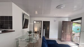 Ein moderner Wohnraum mit einem Glastisch, weißen Stühlen, einem blauen Sofa und einem durchgehenden Durchgang zur Küche.