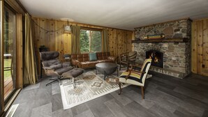 Una sala de estar acogedora con chimenea de piedra, mobiliario de cuero y un ventanal grande.